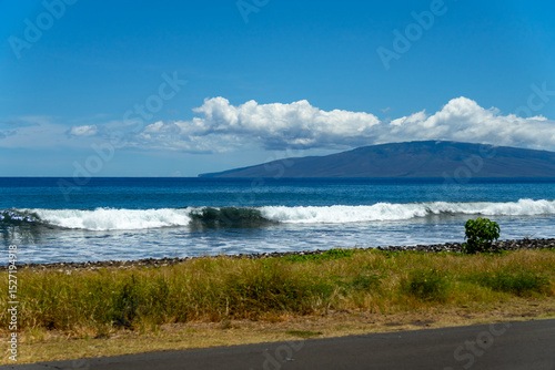 Ocean waves crash on a rocky beach with a mountain in the background.