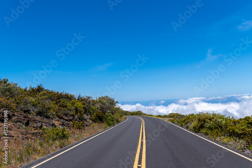 A winding road leads to a horizon of clouds under a clear blue sky.