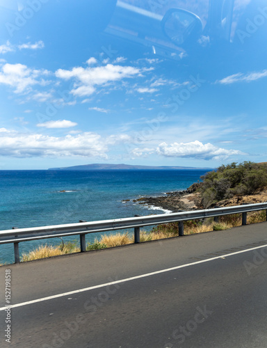 Coastal road view of the ocean and island under a blue sky with clouds.