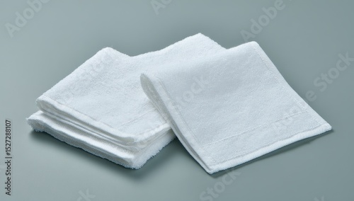 Two white, folded hand towels on a neutral background