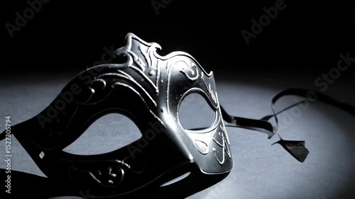 Elegant black masquerade mask with ornate filigree resting on a dimly lit surface with ribbon ties, creating a mysterious atmosphere.