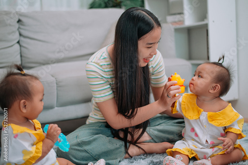 Wallpaper Mural Portrait of Young Asian mother shares a happy moment with her twin daughters while sitting on a soft carpet in a cozy room at home. Leisure activities with family Torontodigital.ca