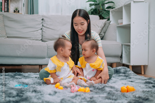 Wallpaper Mural Portrait of Young Asian mother shares a happy moment with her twin daughters while sitting on a soft carpet in a cozy room at home. Leisure activities with family Torontodigital.ca