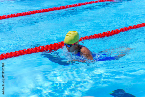 Swimmer child swims breaststroke swimming style in a race swimming pool. Water sports and competition, learning to swim classes for children.