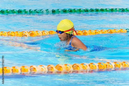 Swimmer child swims breaststroke swimming style in a race swimming pool. Water sports and competition, learning to swim classes for children.
