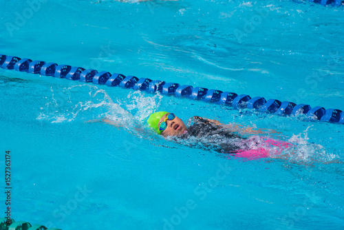 Swimmer child swims backstroke swimming style in a race swimming pool. Water sports and competition, learning to swim classes for children.
