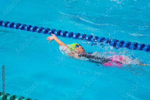 Swimmer child swims backstroke swimming style in a race swimming pool. Water sports and competition, learning to swim classes for children.
