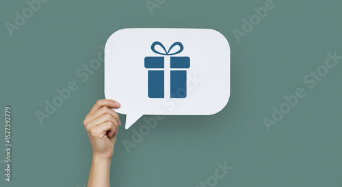 A hand holding a white speech bubble with a blue gift box icon against a green background plain studio business.selling ,purchasing,agreement 