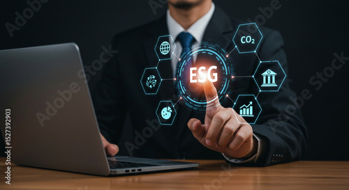 Man in suit using laptop with esg icons floating around his hand on a wooden table surface business.selling ,purchasing,agreement 