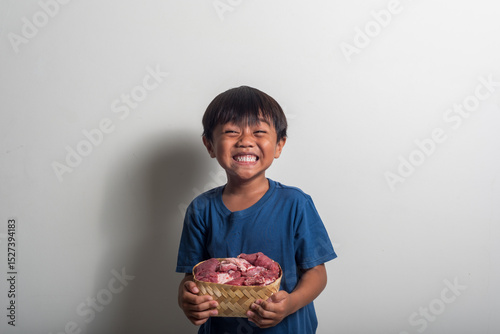 A Smiling Child Holds Raw Meat in a Basket Against a Plain Backg