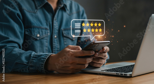 A person using a smartphone with a five star rating graphic and a laptop on a wooden surface nearby business.selling ,purchasing,agreement 