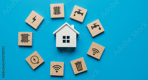 A small white house surrounded by wooden blocks with various utility icons on a blue background view from above business.selling ,purchasing,agreement 