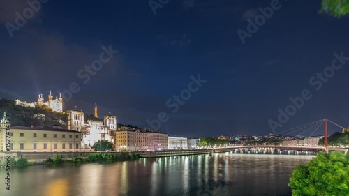 Timelapse of Saint John the Baptist Cathedral and Basilica of Notre-Dame de Fourviere in Lyon, transitioning from day to night. Illuminated waterfront and buildings reflected in the river. France