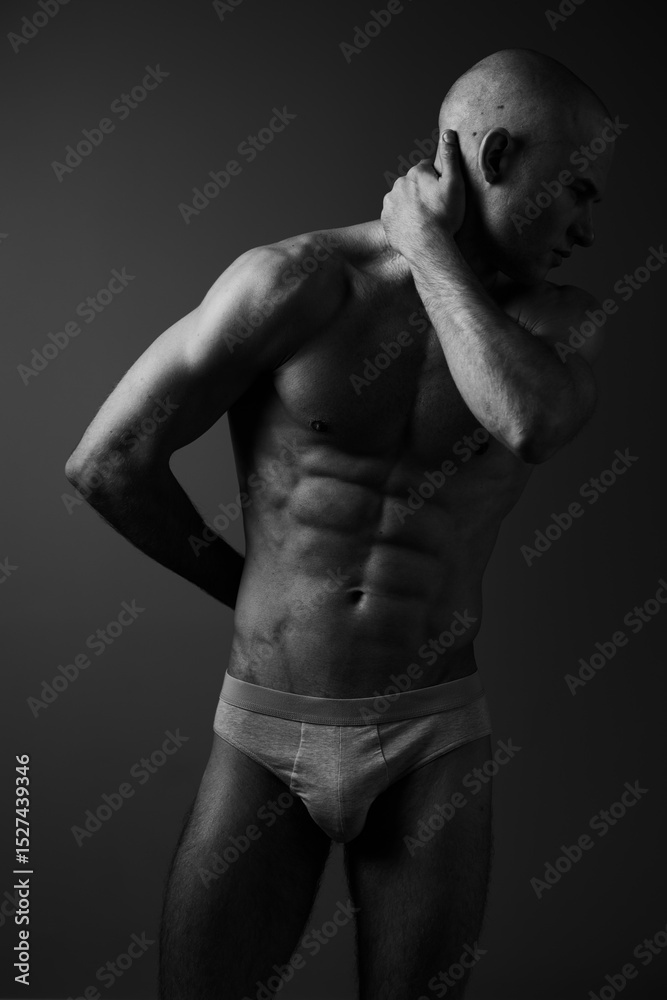 Fototapeta premium Athletic man posing in black and white, showcasing a fit physique and strong emotions. The dramatic lighting enhances the contours and features of his body.