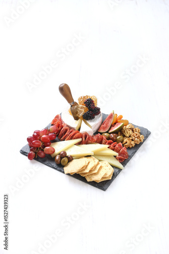 Gourmet charcuterie and cheese board on slate. Assorted cheeses, cured meats, fruits, nuts, and crackers.