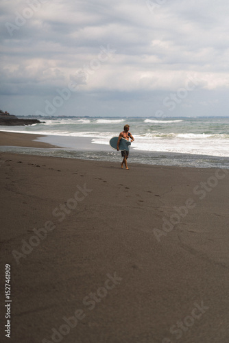 Surfer walking along black sand beach under moody skies