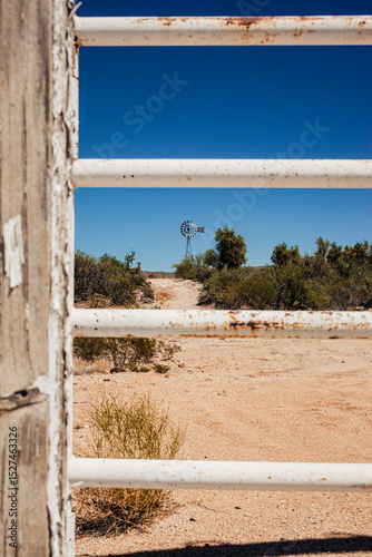 Western scene of windmill through white metal gate bars