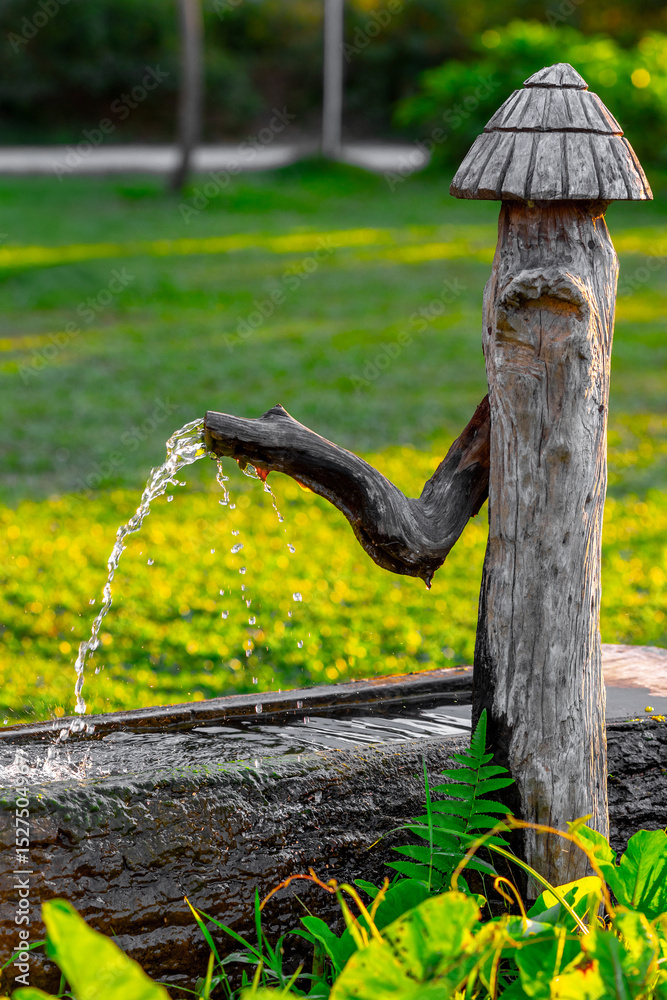 Fototapeta premium Rustic wooden water fountain in lush green garden setting