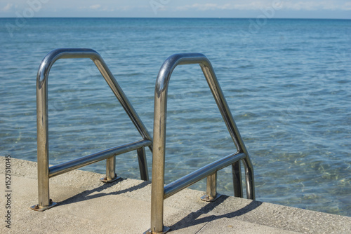 shining metal handrails descending into clear blue sea water, serene coastal view, spacious background, ample copyspace for text, concept of vacation access, relaxation, seaside resort