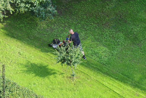 Aerial view of an unknown man mowing the lawn in the morning - green grass and maintenance work in a green area.