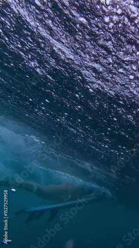 Mid adult female surfer makes duck dive in transparent water of Indian Ocean. Wide angle underwater shot. Vertical video