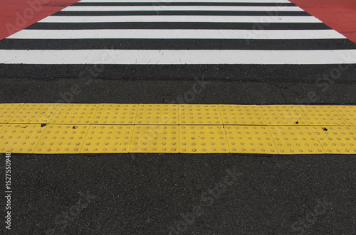 Yellow blocks of tactile paving for blind handicap in front of the pedestrian crossing on the road and the red asphalt. Tactile pavement for the visually impaired background.
