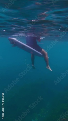Video of male surfer sitting on his surfboard in ocean at cloudy day. Wide angle underwater view. Vertical video