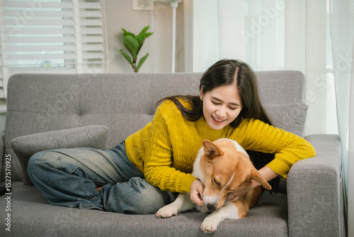 Картината върху платно A young woman relaxes indoors on a cozy sofa, smiling as she bonds with her playful dog, enjoying peaceful companionship at home