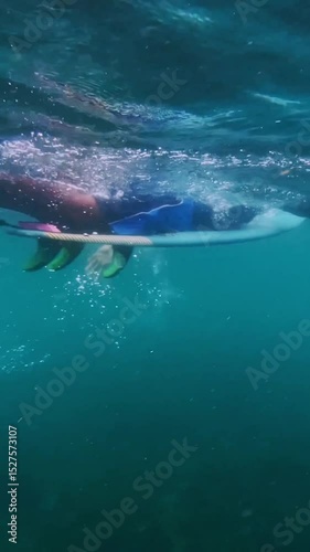Mid adult surfer paddling on his surfboard in Indian Ocean. Underwater slow motion video. Vertical shot