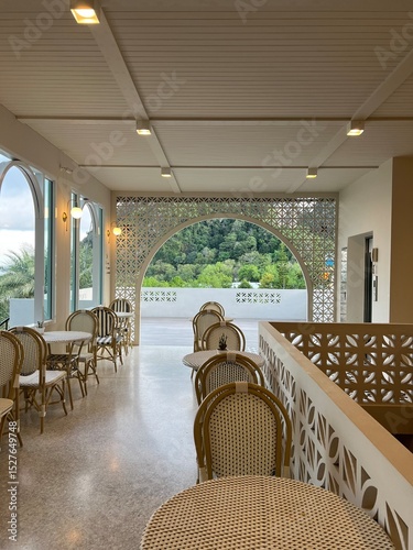 Editorial image. Restaurant Terrace with Mountain View. Elegant restaurant terrace featuring wicker dining chairs and decorative geometric screens with scenic mountain lan. Krabi, Thailand. April 2025