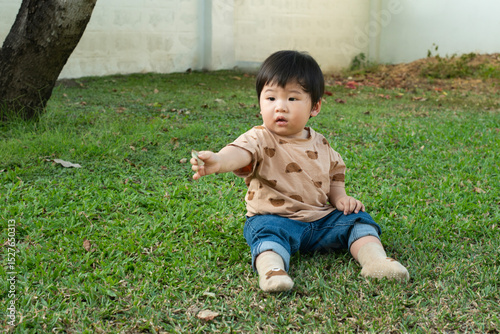 Asian baby boy sitting and playing on green grass