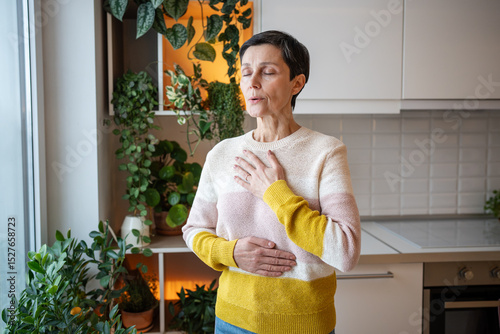 Foto Content serene older woman practicing deep breaths in meditation, hands on torso at home