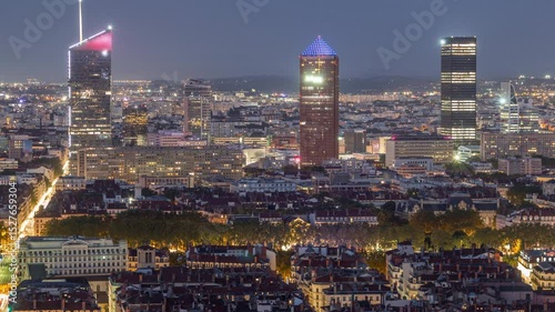 Panoramic aerial view of Lyon after sunset from Fourviere Hill day to night transition. The skyline features skyscrapers surrounded houses and iconic city landmarks illuminated in warm evening