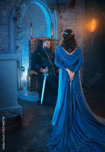 beauty Queen rear view medieval royal creative dress clothes. Lady holds gothic dagger behind back. Blue cloak cape. Backdrop old retro room. Strong adult men king sits on throne Dangerous conspirator photo