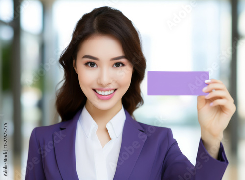 Young businesswoman holds a blank card and smiles confidently in a modern office environment with natural light