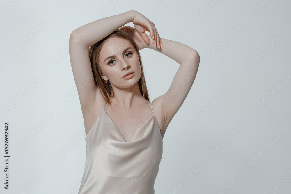 Fototapeta premium Young woman poses gracefully against a neutral background in minimalist fashion attire during a studio shoot