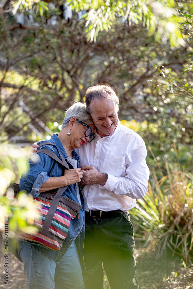 Senior woman resting her head on man's chest while walking in public park Senior woman resting her head on man's chest while walking in public park