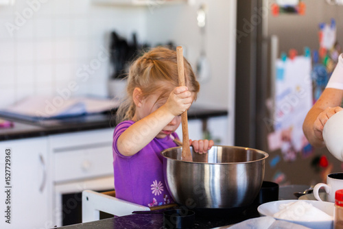 Child in kitchen mixing bowl with huge spoon baking with mum photo