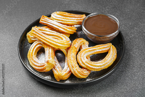 Traditional spanish dessert churros, fried dough pastry dusted with powdered sugar and chocolate sause on black background. Street food, sweet snack, homemade dessert.