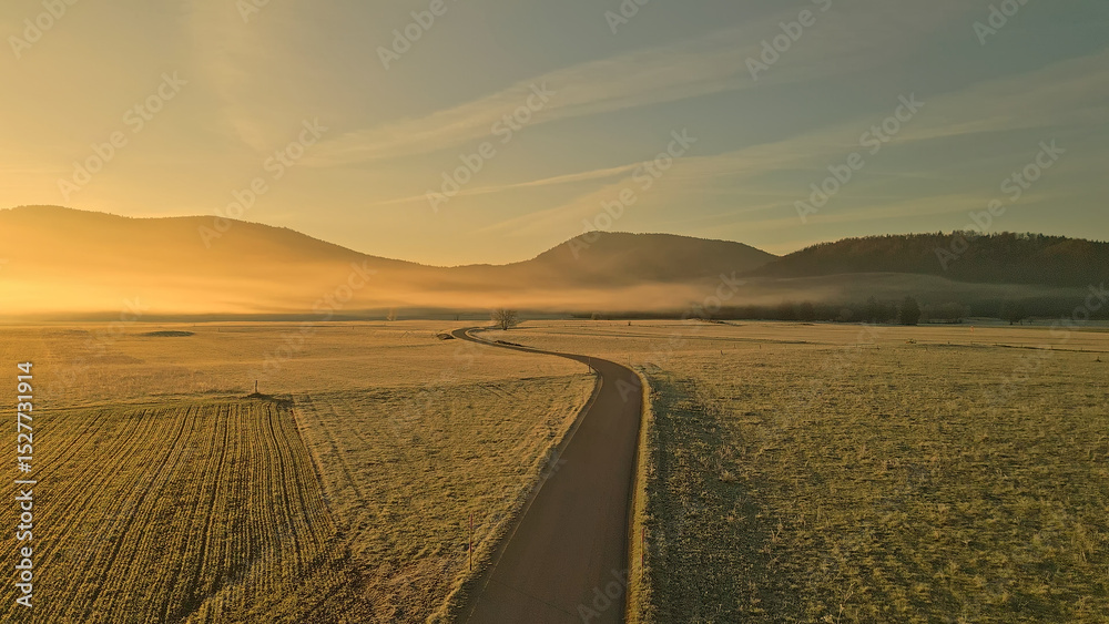 Fototapeta premium An aerial view of a winding road through a vast, foggy field with distant mountains, creating a serene and peaceful atmosphere for outdoor enthusiasts and cyclists.