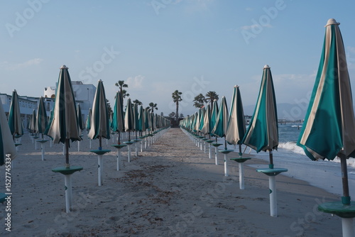 Fototapeta Naklejka Na Ścianę i Meble -  Closed umbrellas on sandy beach in Sardinia, Poetto shore with summer mood and calm coastal atmosphere