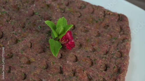 Kebbe naye is showcased on a white plate, featuring finely chopped raw meat mixed with bulgur, onions, mint, and spices, designed for a rich culinary experience.