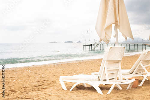 Fototapeta Naklejka Na Ścianę i Meble -  Beach scene with empty closed umbrellas and sun loungers on on sea shore