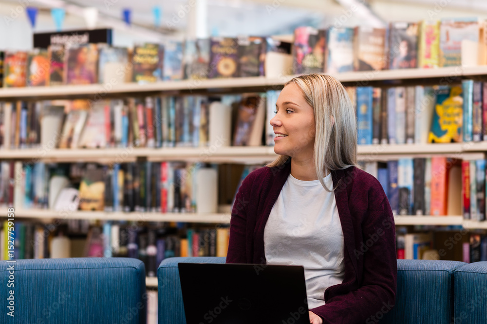 Young Australian Student in library studying on laptop surrounded by bookshelves of books Young Australian Student in library studying on laptop surrounded by bookshelves of books