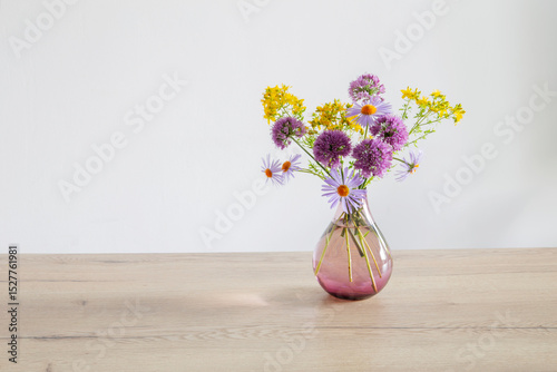 purple and yellow flowers in glass modern vase on wooden table