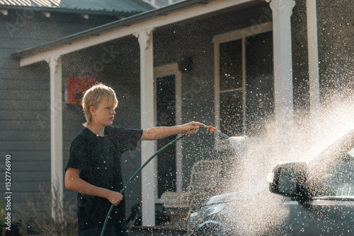 Teenage boy hosing down vehicle in preparation for cleaning car