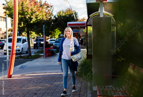 Australian young woman walking down sidewalk in urban area of country town in autumn