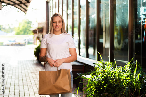 Australian young woman walking down footpath in urban area of town holding brown shopping bag