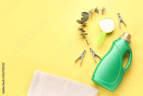 Laundry detergents, folded towel and eucalyptus branch on yellow background