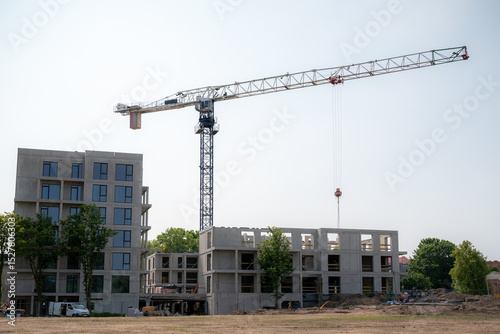 A construction site features a large tower crane with a long horizontal jib extending over partially constructed buildings. 